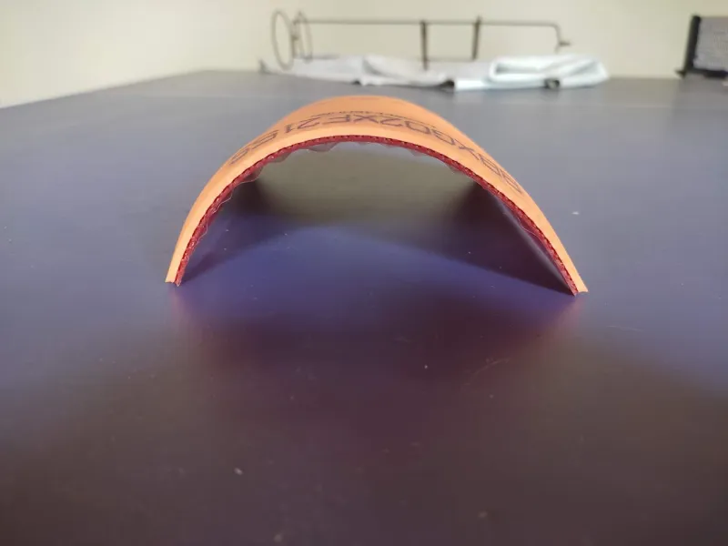 DHS Hurricane 3 National table tennis rubber curled into a dome, showing the tacky orange topsheet and red sponge
