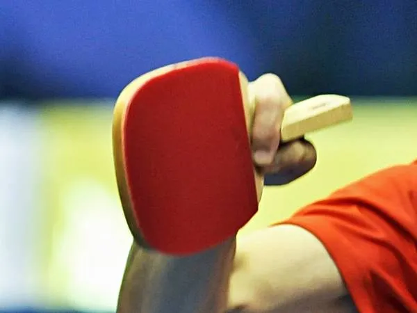 Red Japanese-style penhold table tennis paddle held in forehand position with thumb and index finger grip