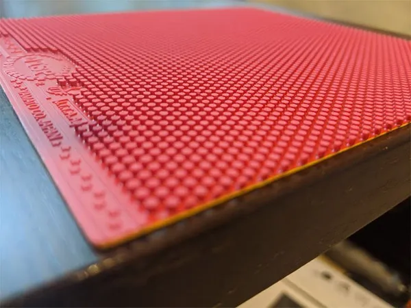 Side-angle close-up of a red long pimples table tennis rubber attached to a blade, showing the elongated pip structure