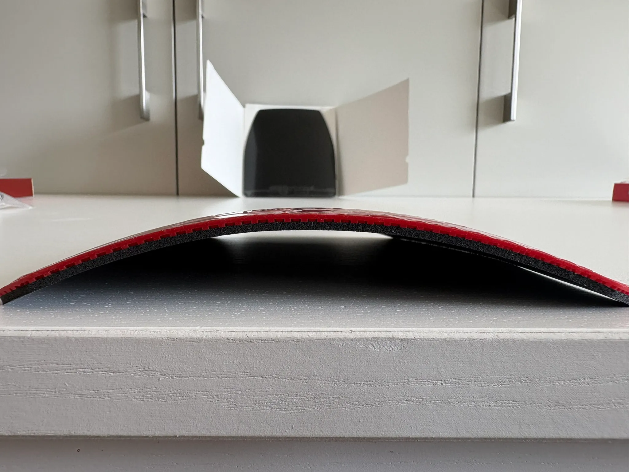 Side profile of a Sanwei Target Europe Soft sheet curving upward on a white surface, showing pronounced factory curl.