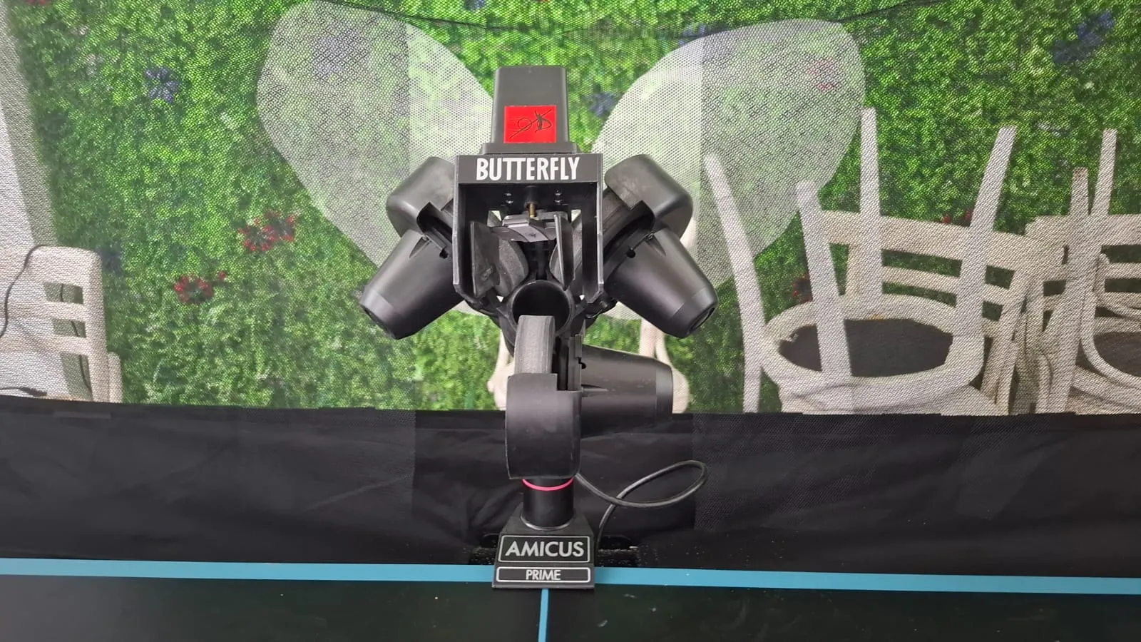 Wide front view of the Butterfly Amicus Prime mounted on a table with the recycling net in the background and a green leafy wall behind.