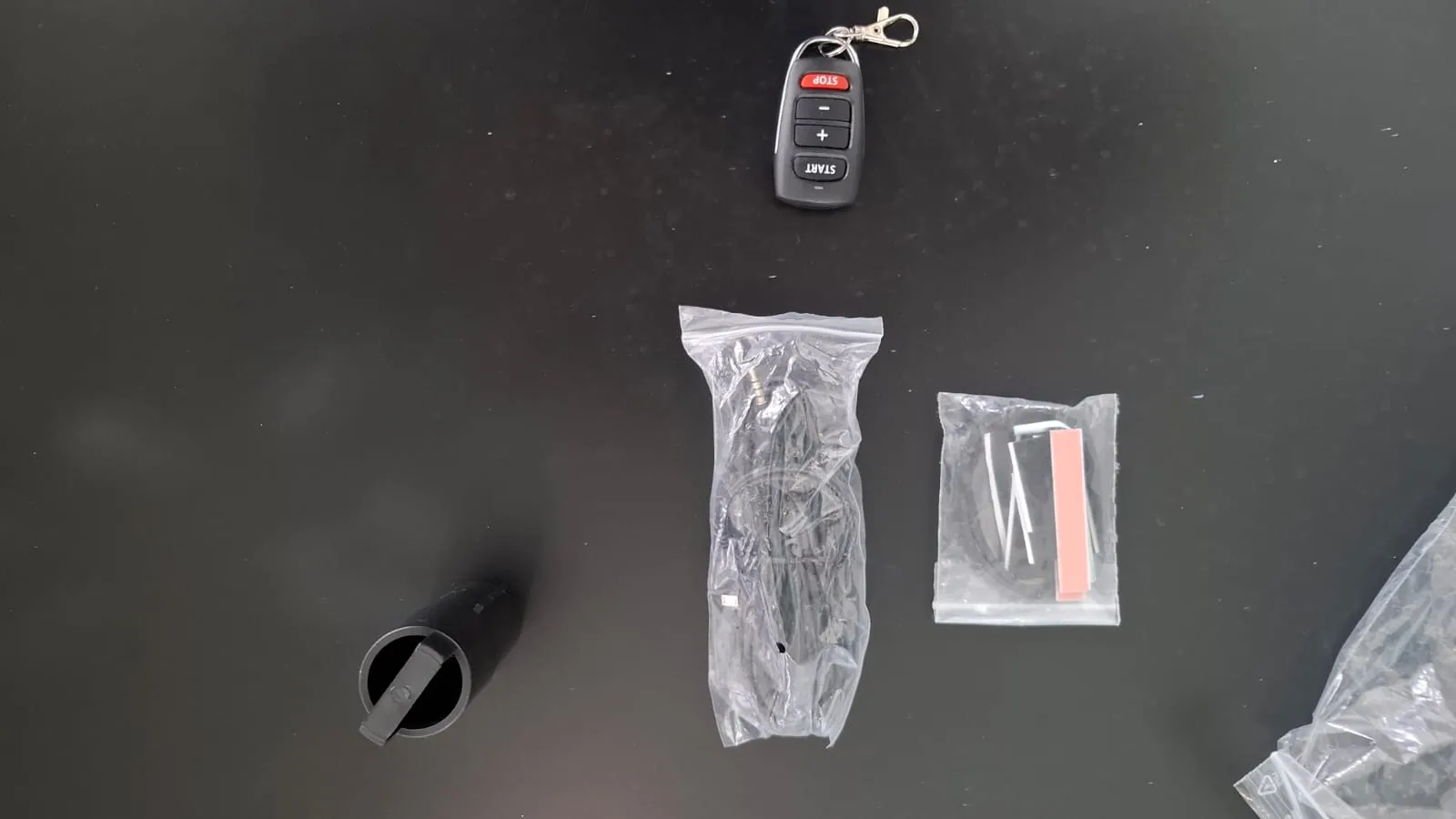 Butterfly Amicus Prime accessories laid out on a black table including the wireless remote, charging cable in a clear bag, and a smaller accessory bag with hardware and adjustment tools.