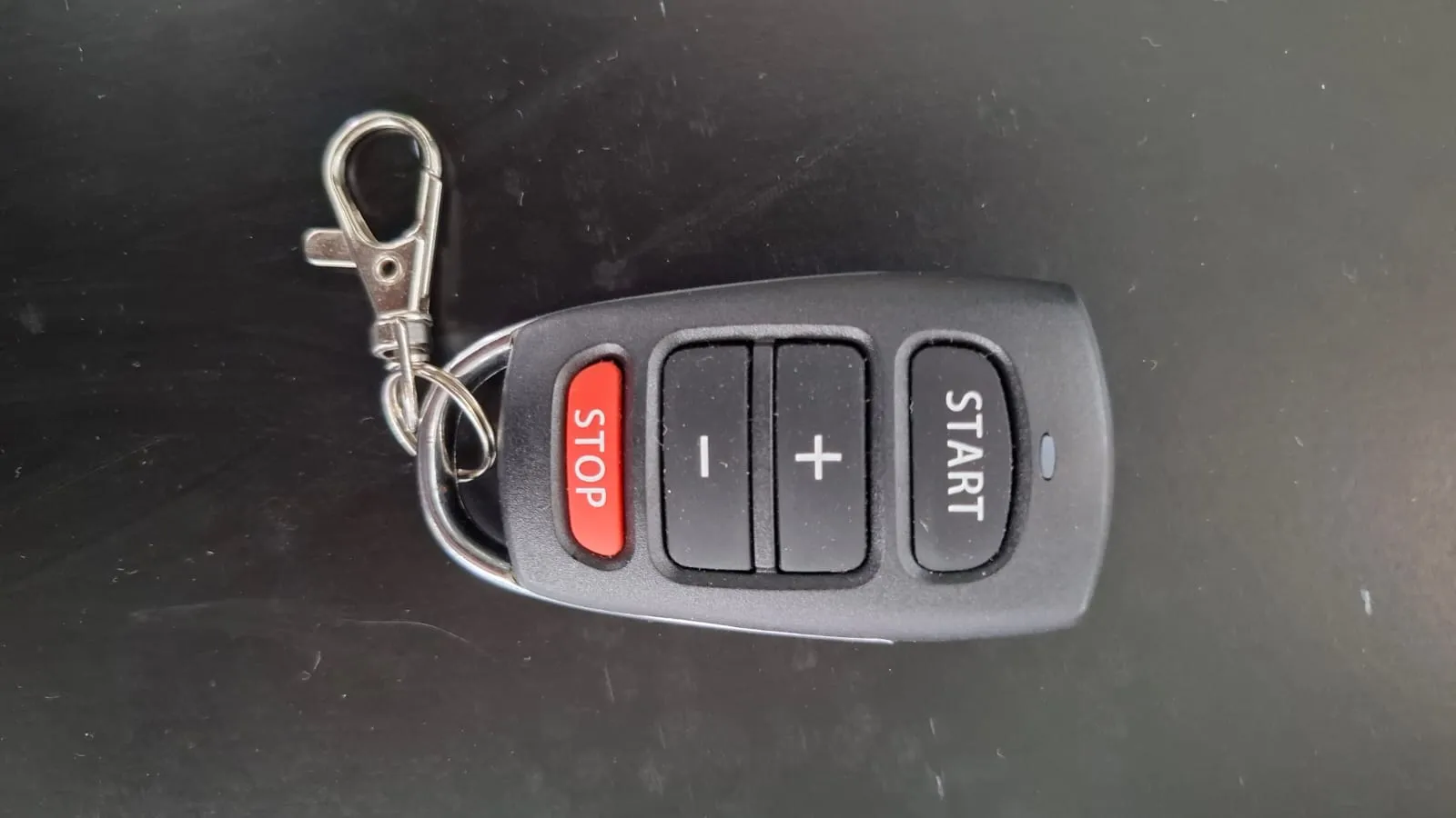 Wireless remote control for the Butterfly Amicus Prime with red Stop button, plus and minus buttons, and Start button, attached to a metal keyring.