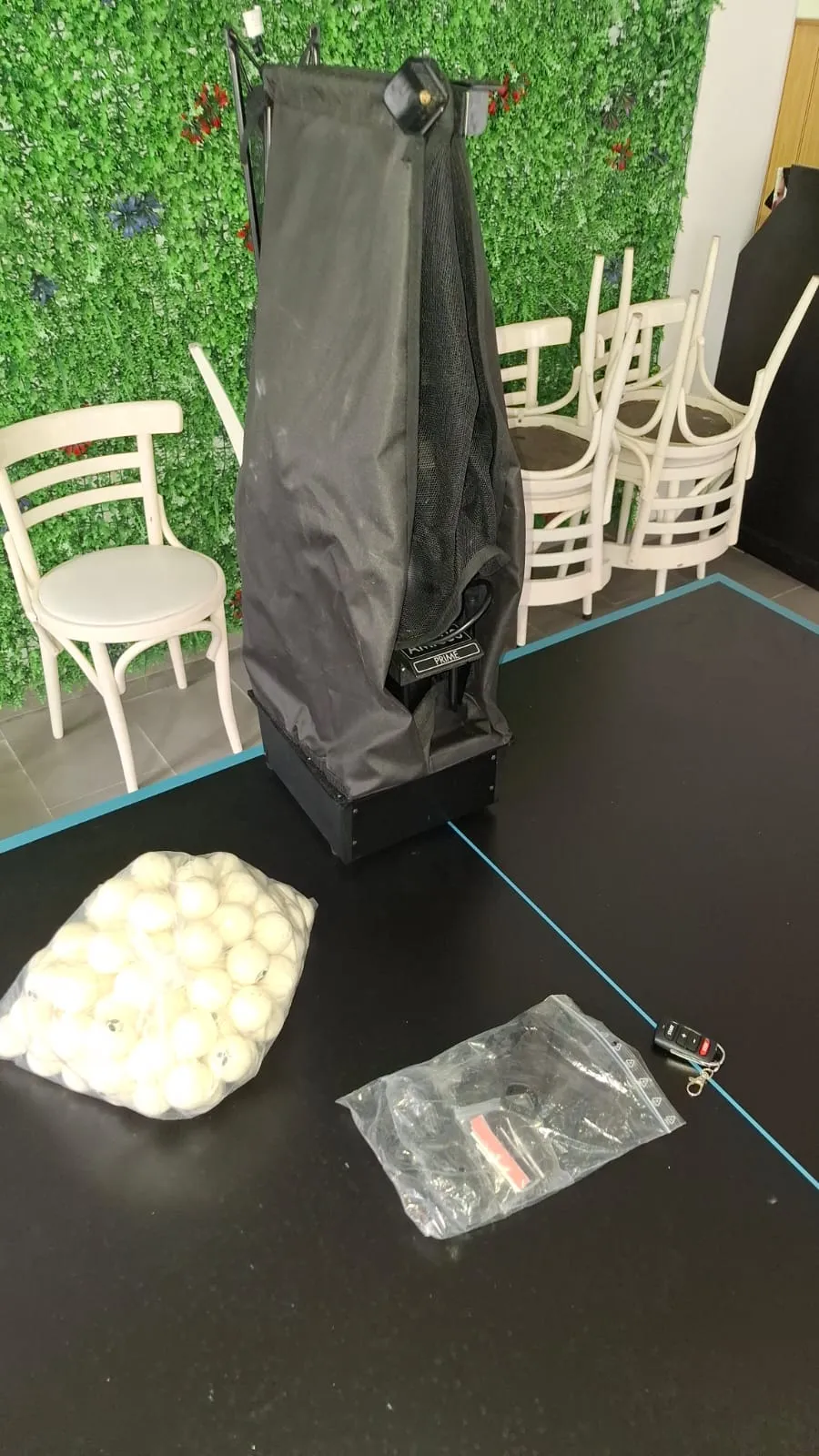 Butterfly Amicus Prime carrying bag standing upright next to a clear bag of white training balls and the accessory pouch on a black table.