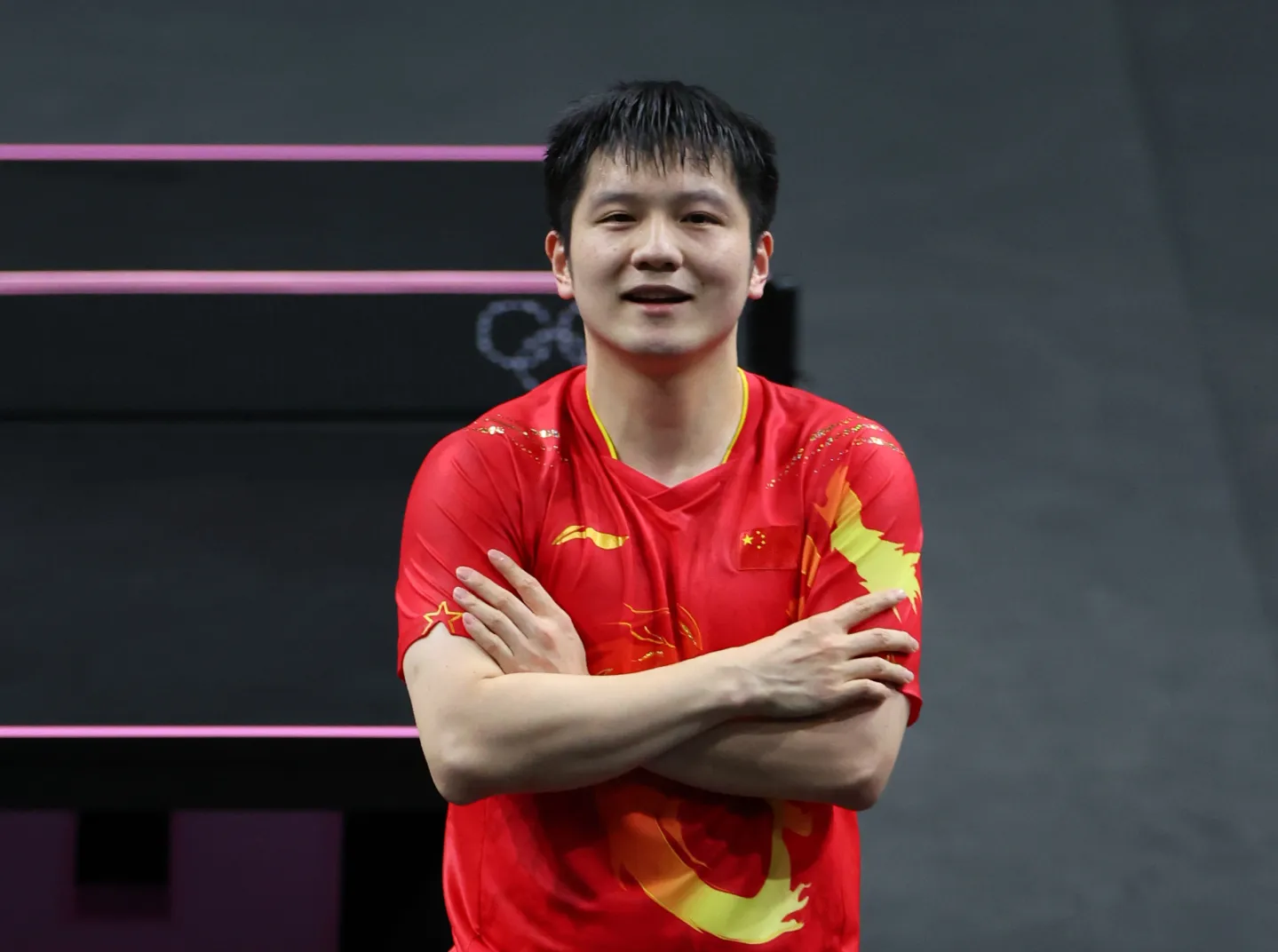 Chinese table tennis player in a red national jersey posing arms-crossed inside the South Paris Arena at the Paris 2024 Olympic Games