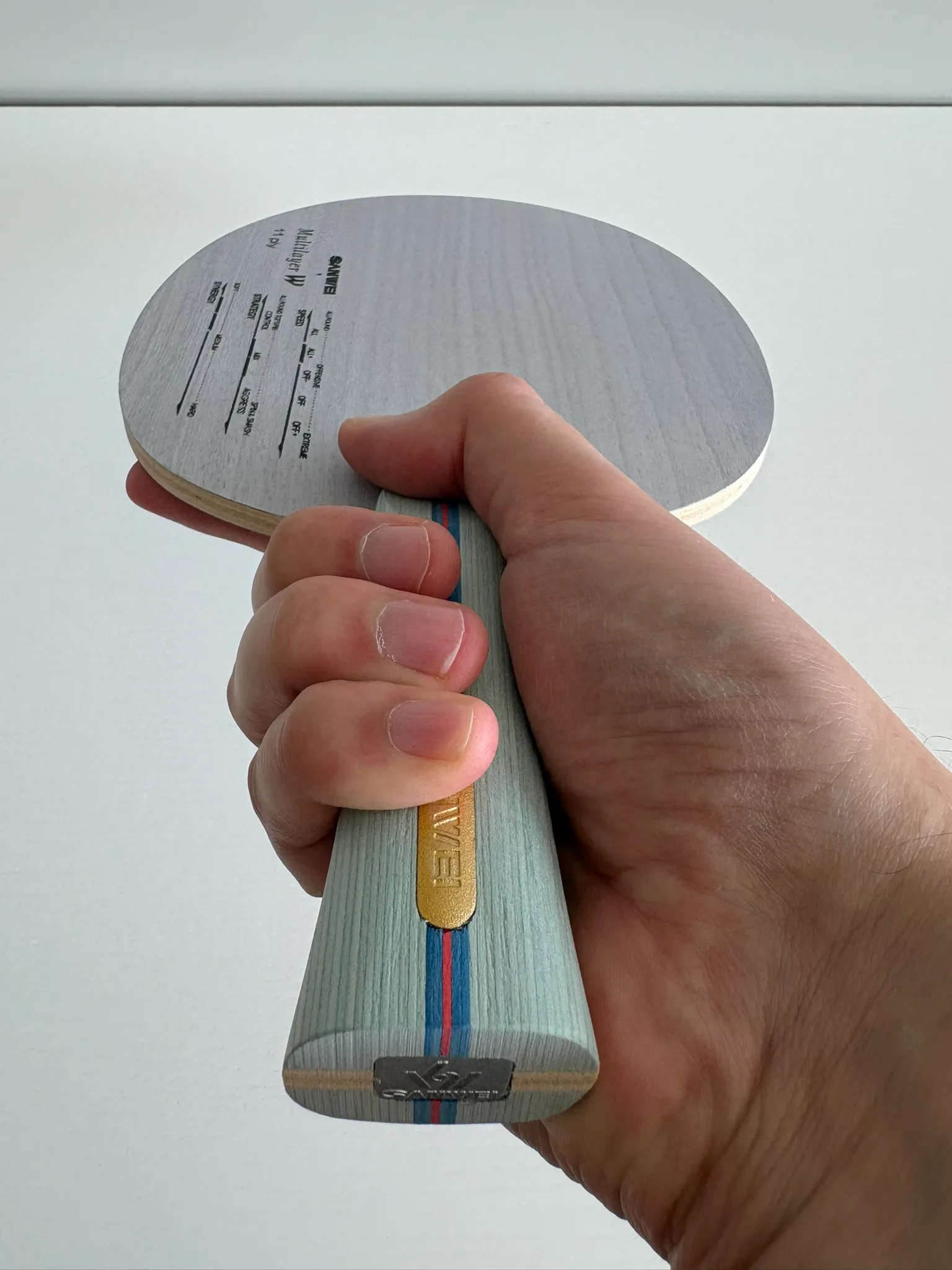 Hand gripping the flared blade handle from below, showing the pale wood and thin blue and red stripes.
