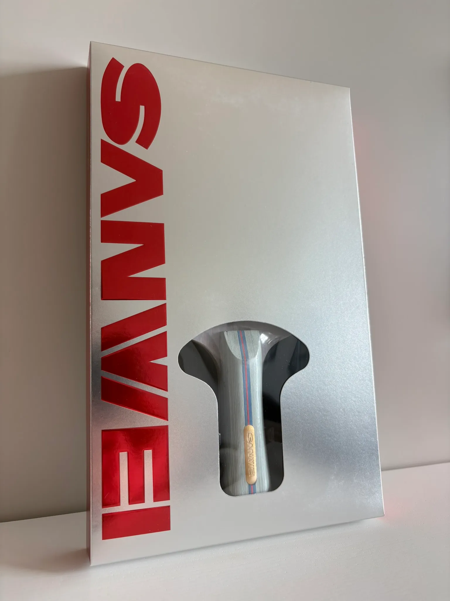 Silver Sanwei retail box standing on a white surface with red foil lettering and a handle-shaped cut-out window.