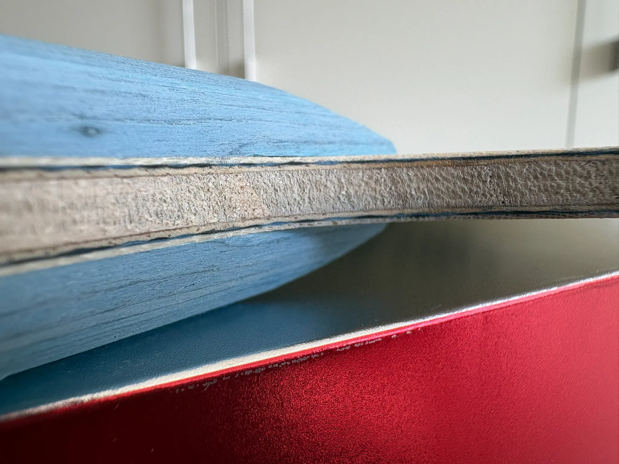Close-up of the Sanwei Pistol Racket edge showing wood and dark composite layers.