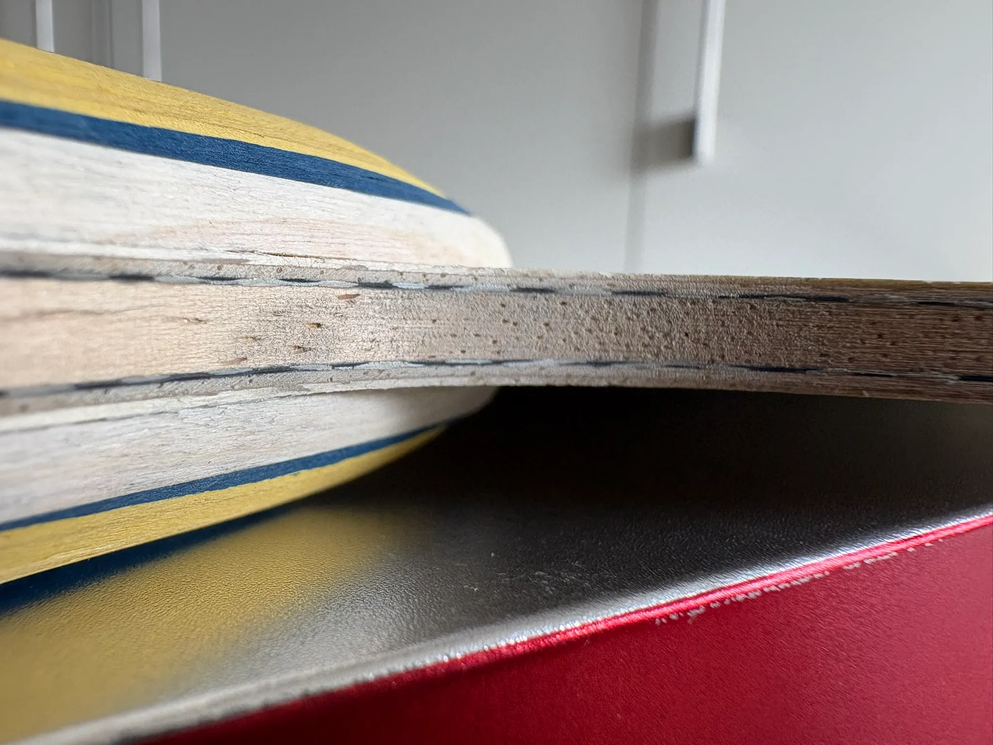 Macro view of the Sanwei Surge Prism blade edge showing the layered wood plies and a darker fibre layer.