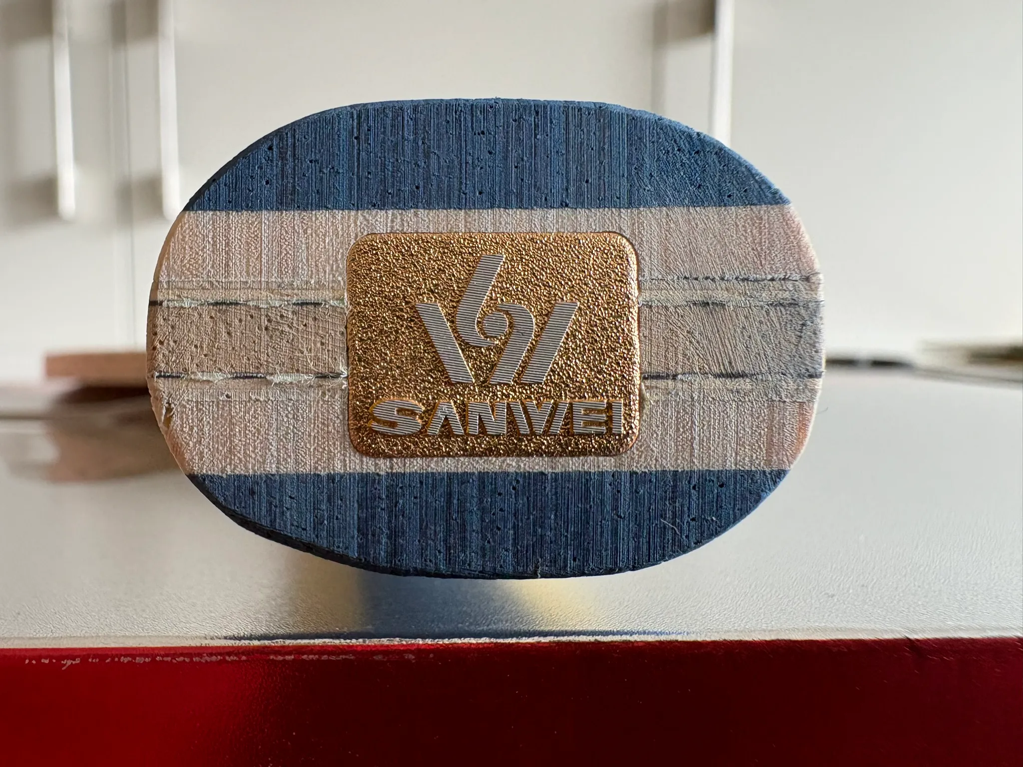 Close-up of the Sanwei Surge Prism handle butt showing the two-tone blue and yellow wood and a gold Sanwei badge.