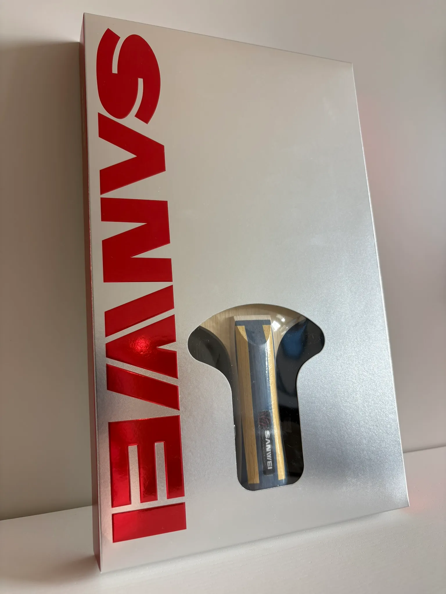 Silver Sanwei retail box standing upright with a cut-out window showing the blade handle inside.