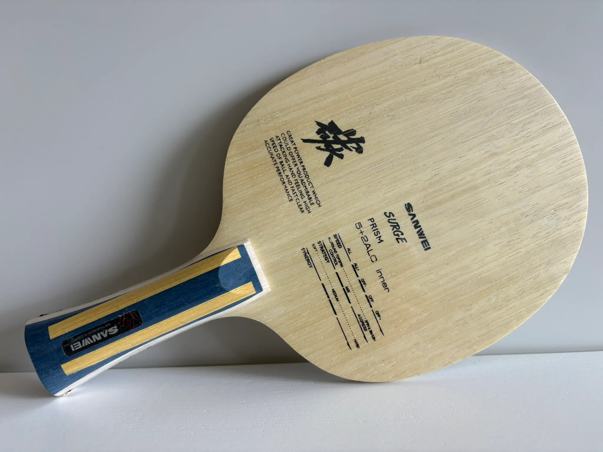 Sanwei Surge Prism laid flat on a white surface with the printed spec chart and branding visible on the light wood face.